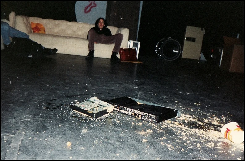 Person on couch in dark room, broken keyboard on floor, scattered debris.