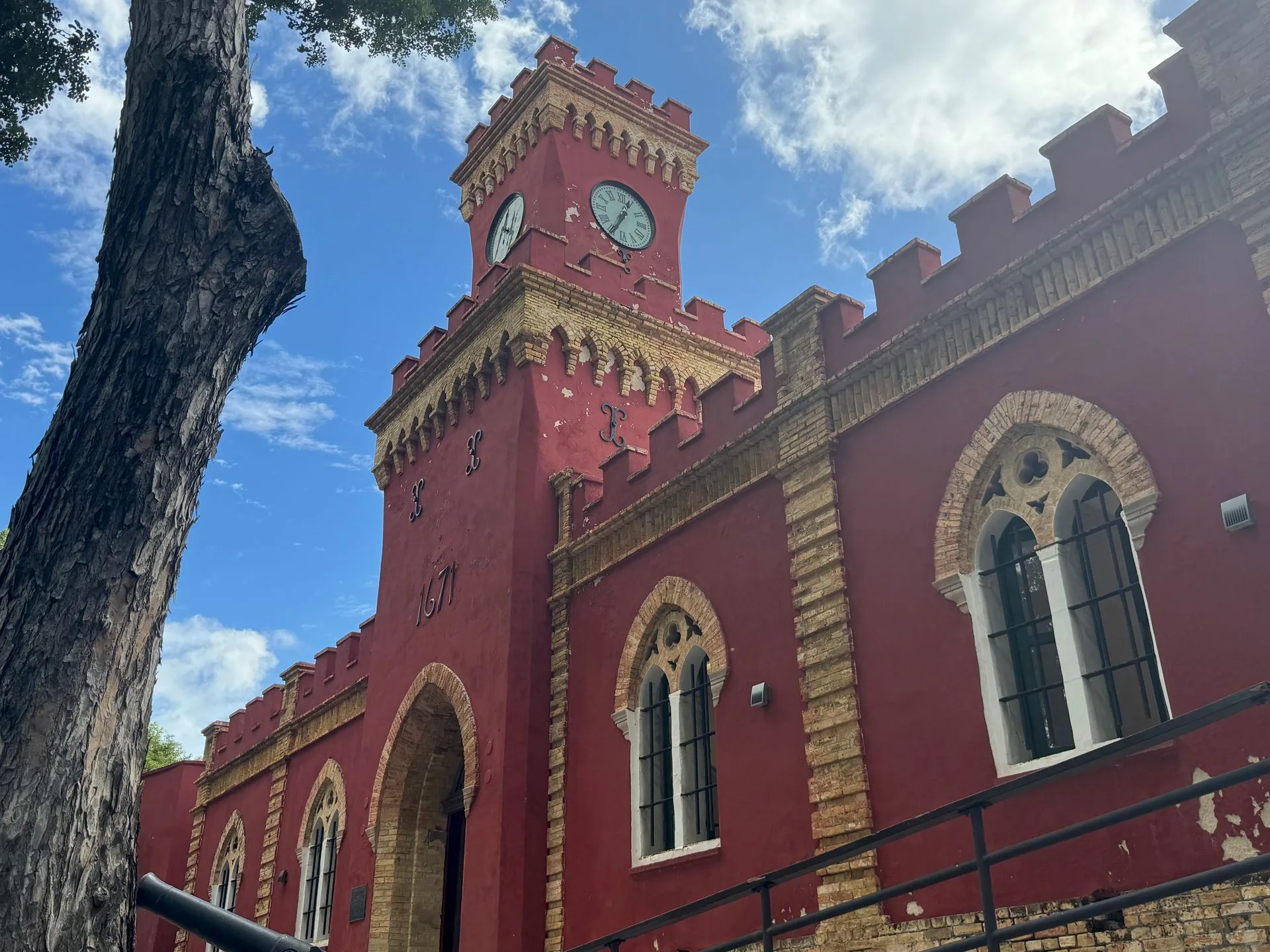 Red historic building with clock tower against a blue sky with clouds.