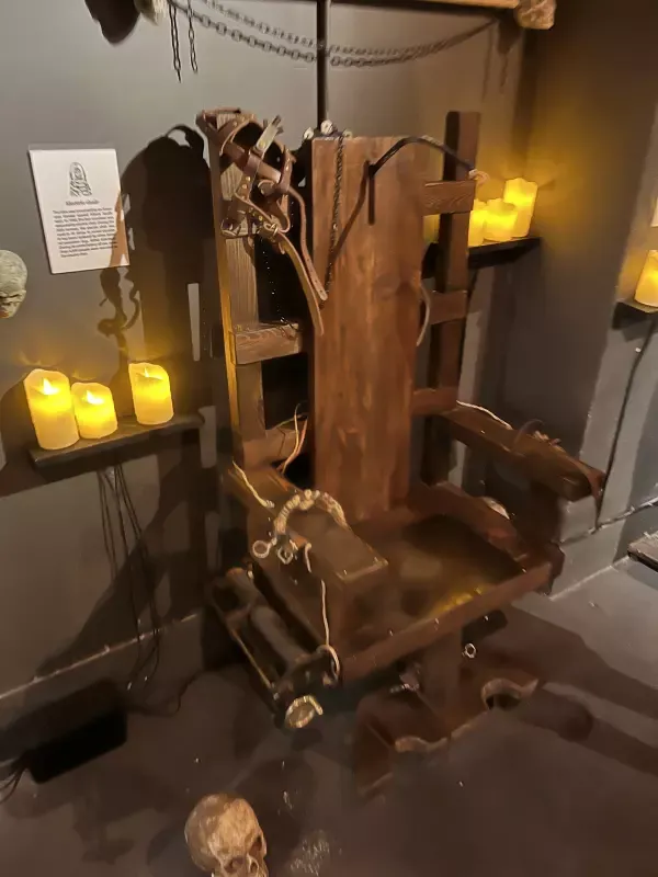 A wooden chair with a skeleton on it is in a room with candles.