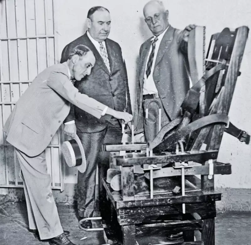 A black and white photo of three men standing around a machine