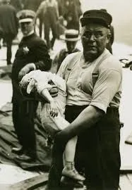 Man holding a child, likely a rescue scene. Black and white, somber faces in a crowd.