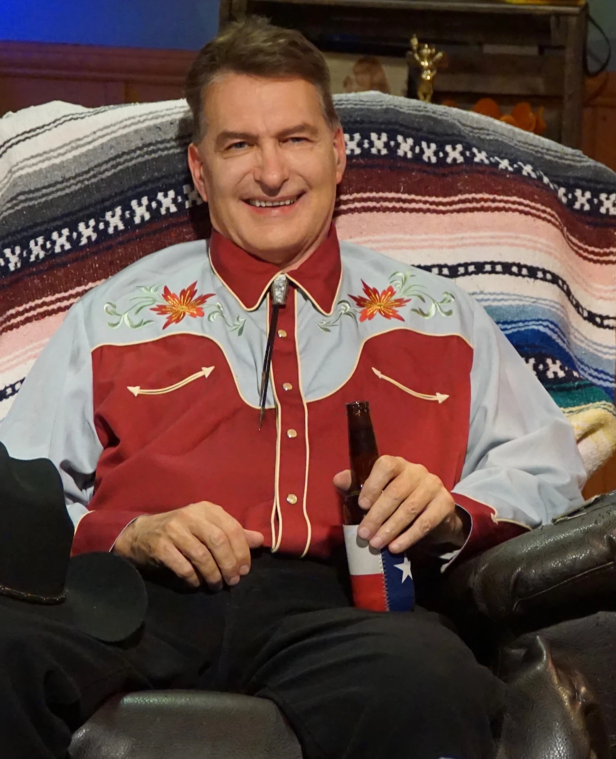 A man in a cowboy shirt is holding a bottle of beer