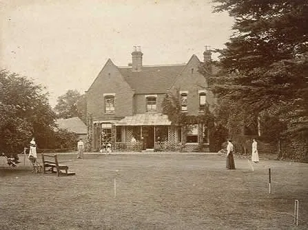 People playing croquet on a lawn in front of a large house. Vintage sepia photograph.