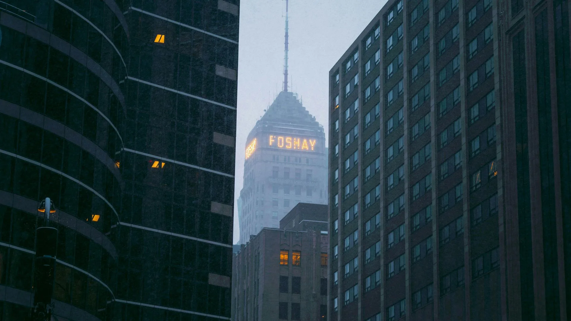 City buildings in the rain, with a tall, illuminated skyscraper in the distance.
