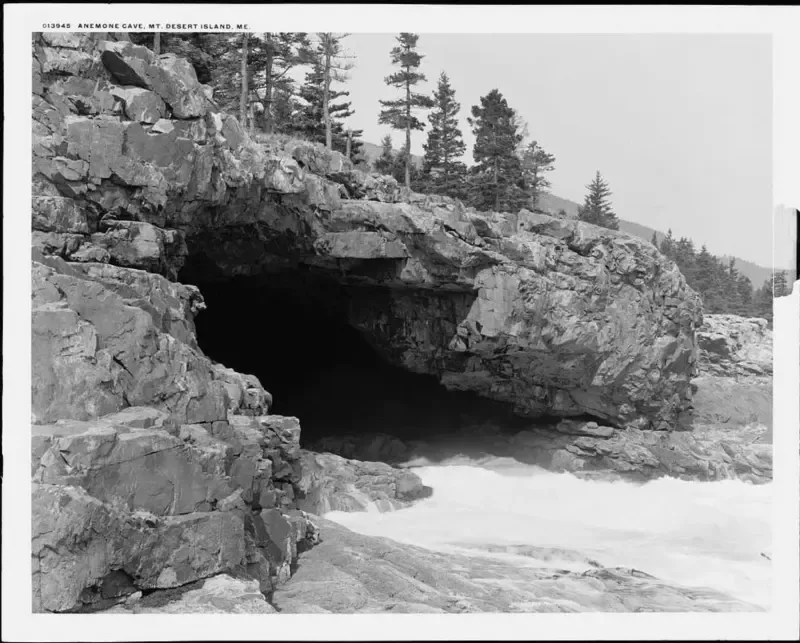 A black and white photo of a cave with trees in the background