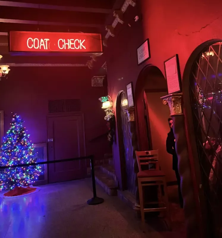 A coat check sign hangs above a christmas tree