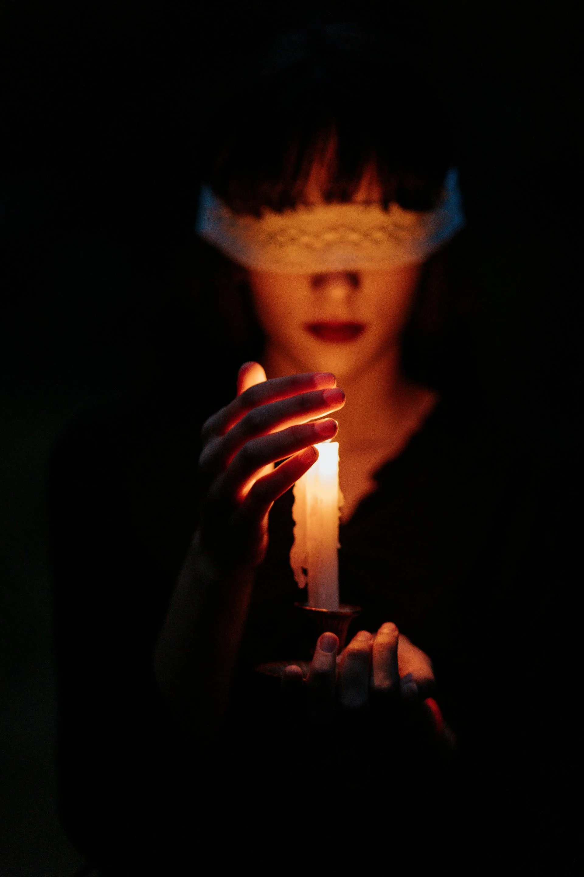Woman with blindfold holds lit candle in dark setting.
