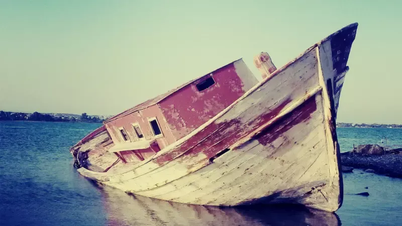 An old wooden boat is floating on its side in the water.