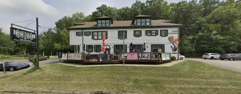 A large white building with a deck in front of it is surrounded by trees.