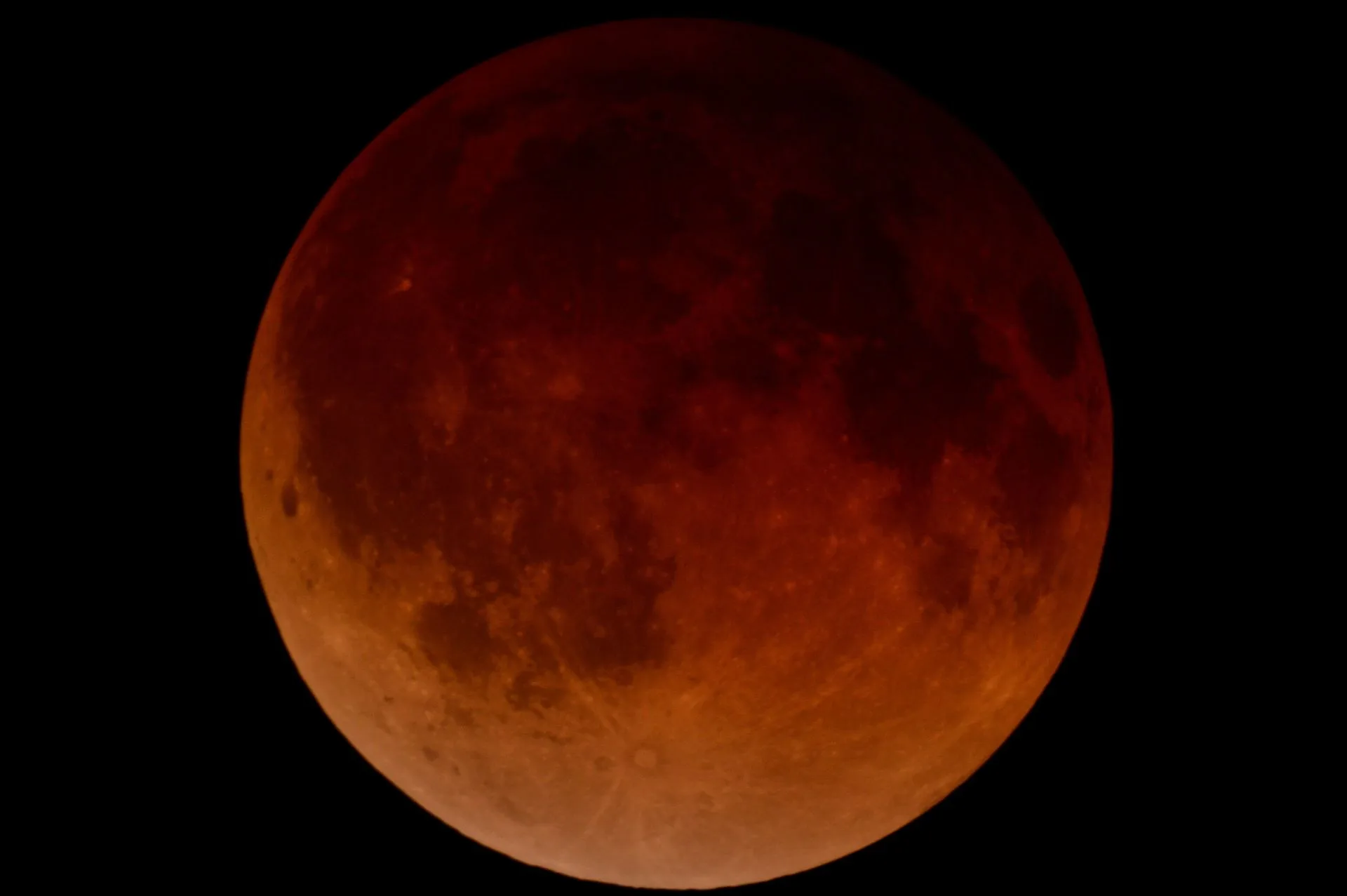 Blood moon during a total lunar eclipse; dark red and orange hues across the lunar surface.