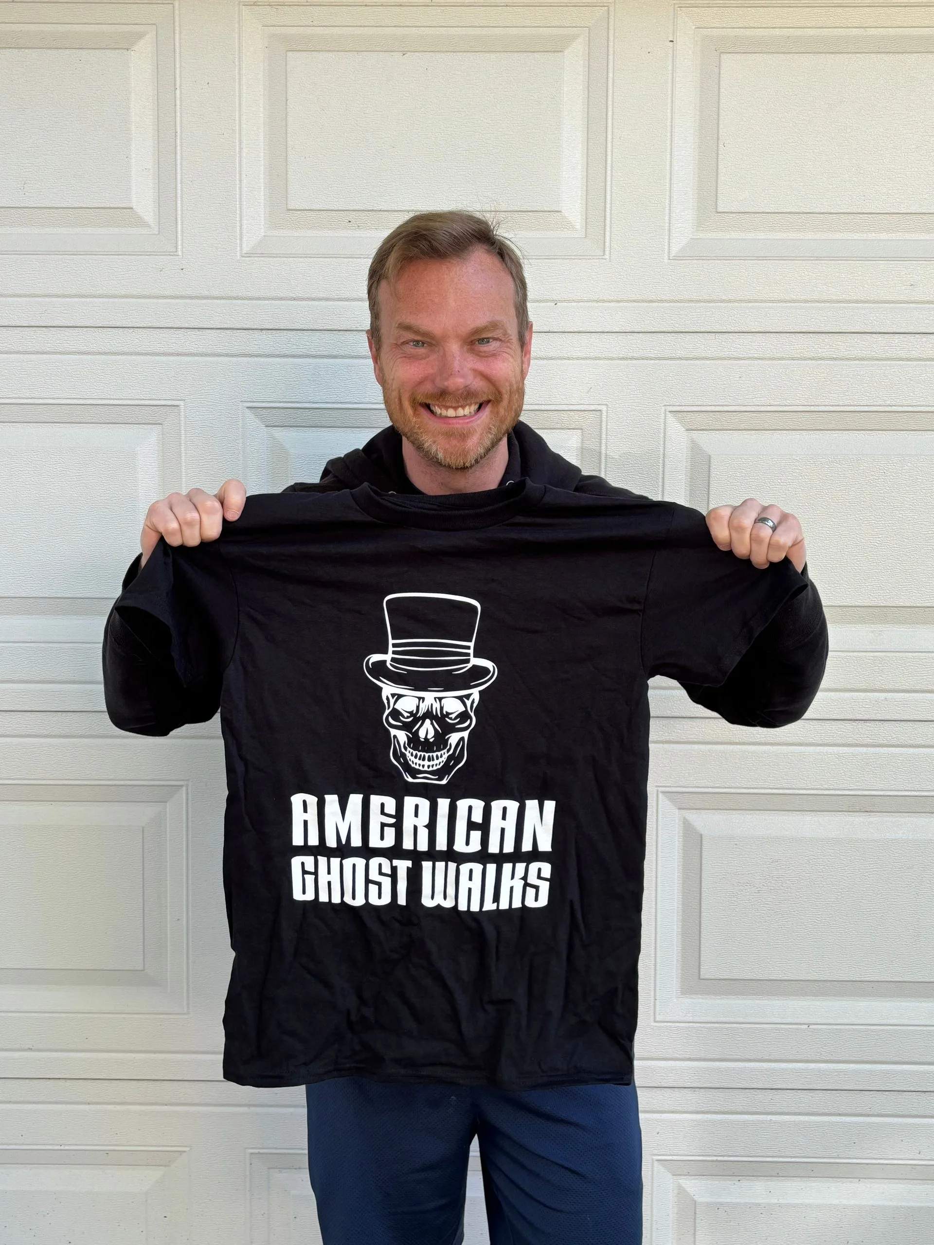 A man is holding a black shirt that says american ghost walks
