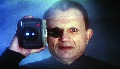 Man staring intensely at camera. Holding a vintage camcorder, blue and black background.