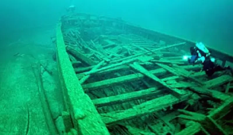 A scuba diver is looking at an old boat wreck in the ocean.