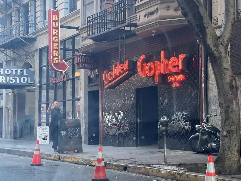 A man walking down a street in front of a restaurant called golden gopher