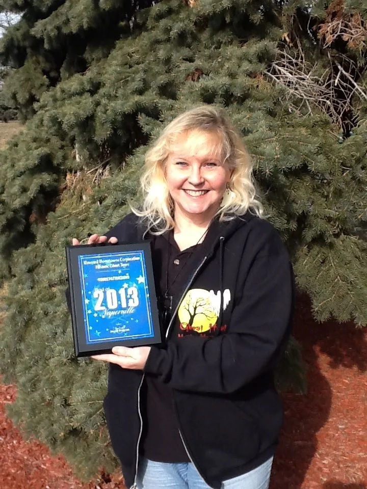 A woman in a black hoodie is holding a plaque that says 2013
