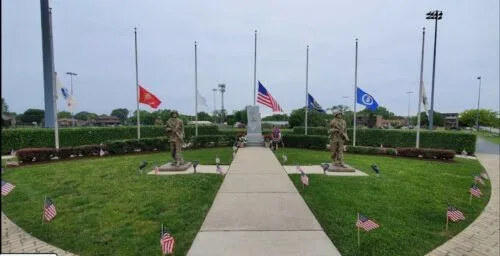 A statue of a soldier stands in the middle of a park surrounded by flags.