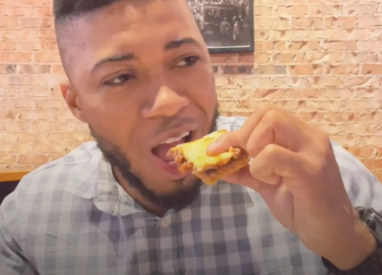A man in a plaid shirt is eating a sandwich