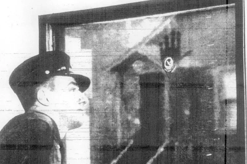 A black and white photo of a man in a hat looking out a window.