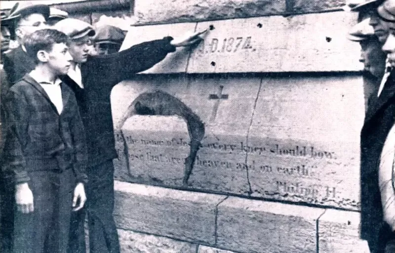 A black and white photo of a group of men pointing at a plaque that says 0.1874